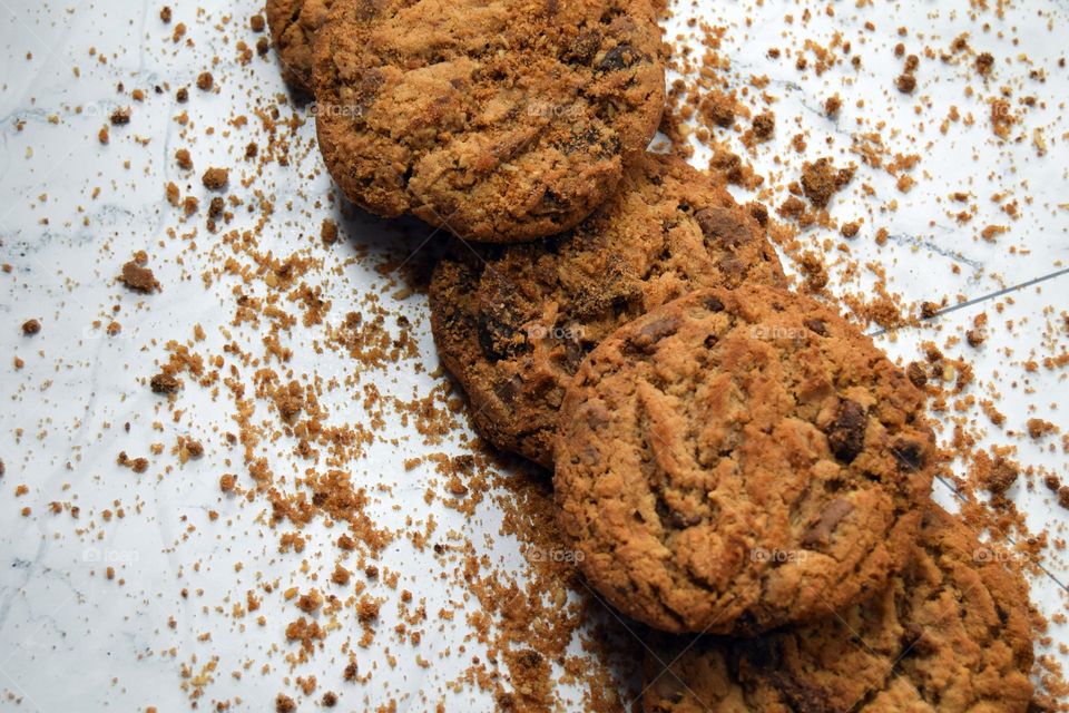A neatly stacked row of delicious looking golden brown chocolate chip cookies surrounded by a sprinkling of chocolate chip cookie crumbs.