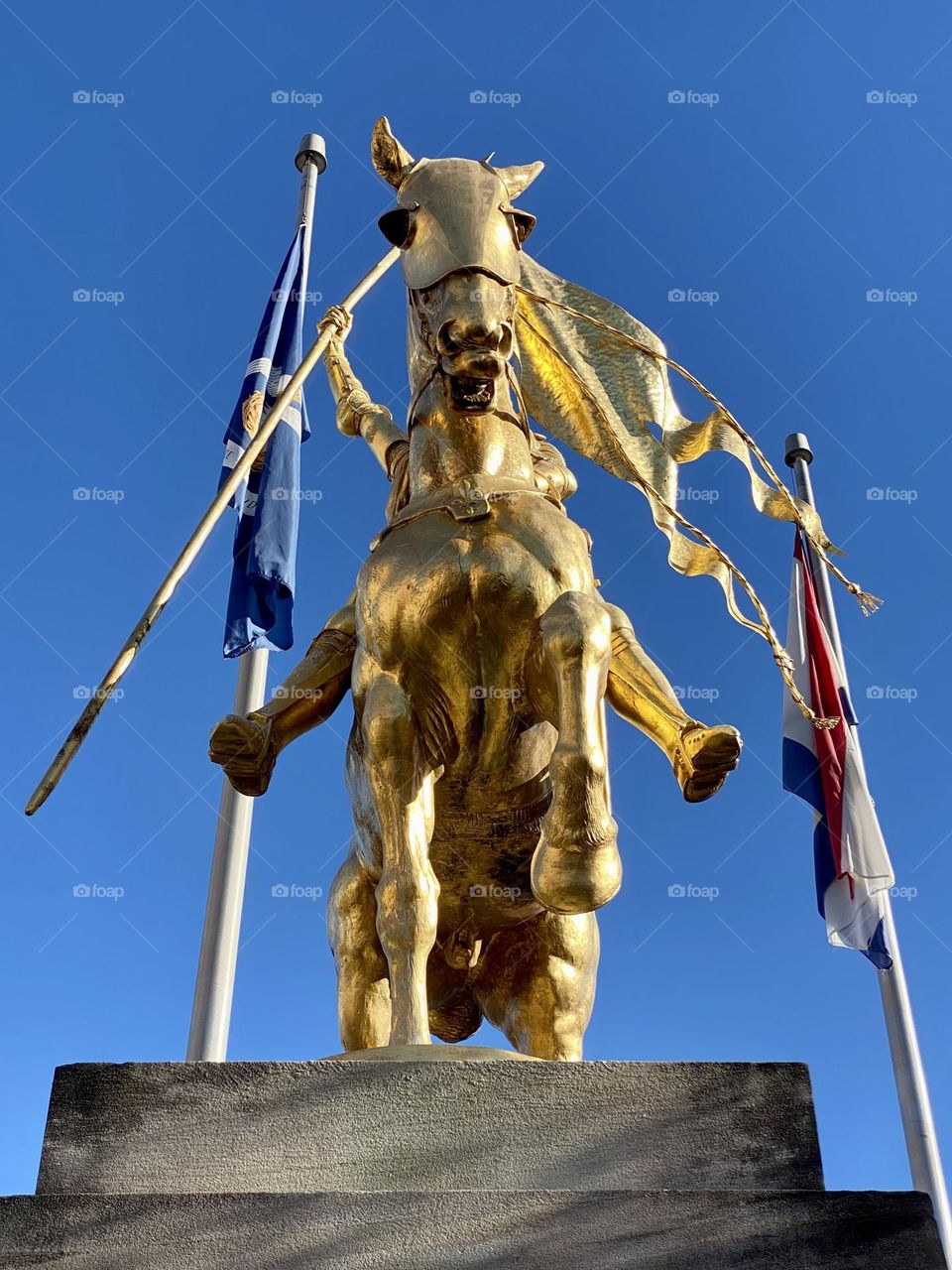 A statue of Joan of Arc with 2 flags in the background