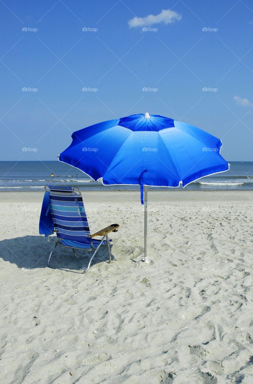 Blue Beach chair and umbrella by the ocean.