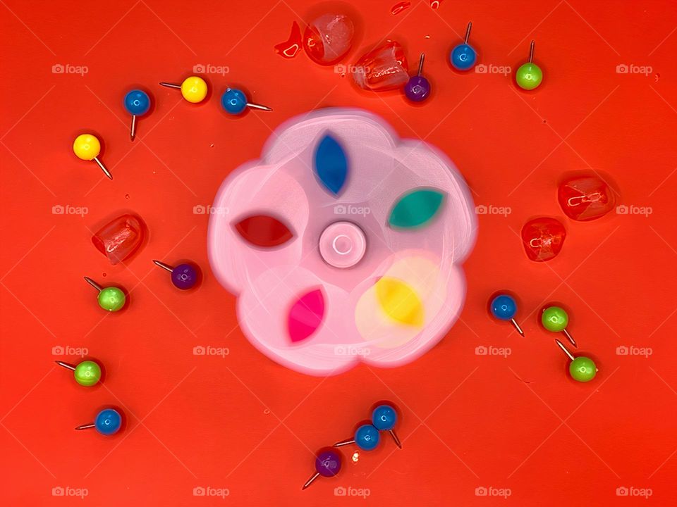 Multicolor Fidget Spinner Time In Motion Long Exposure Seems To create Cold Ice Cubes On A Red Background.