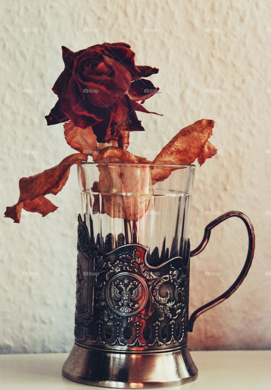 Dried up red rose standing inside a Russian metal glass holder.