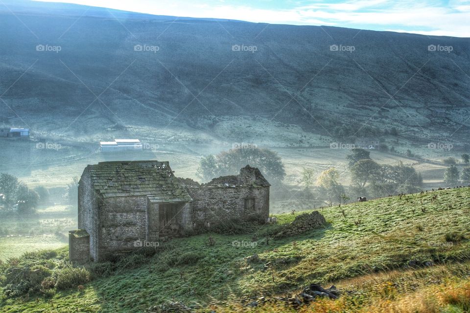 Misty Morning Landscape. A derelict barn sits on the slope of a deep valley on a misty, sunny morning.