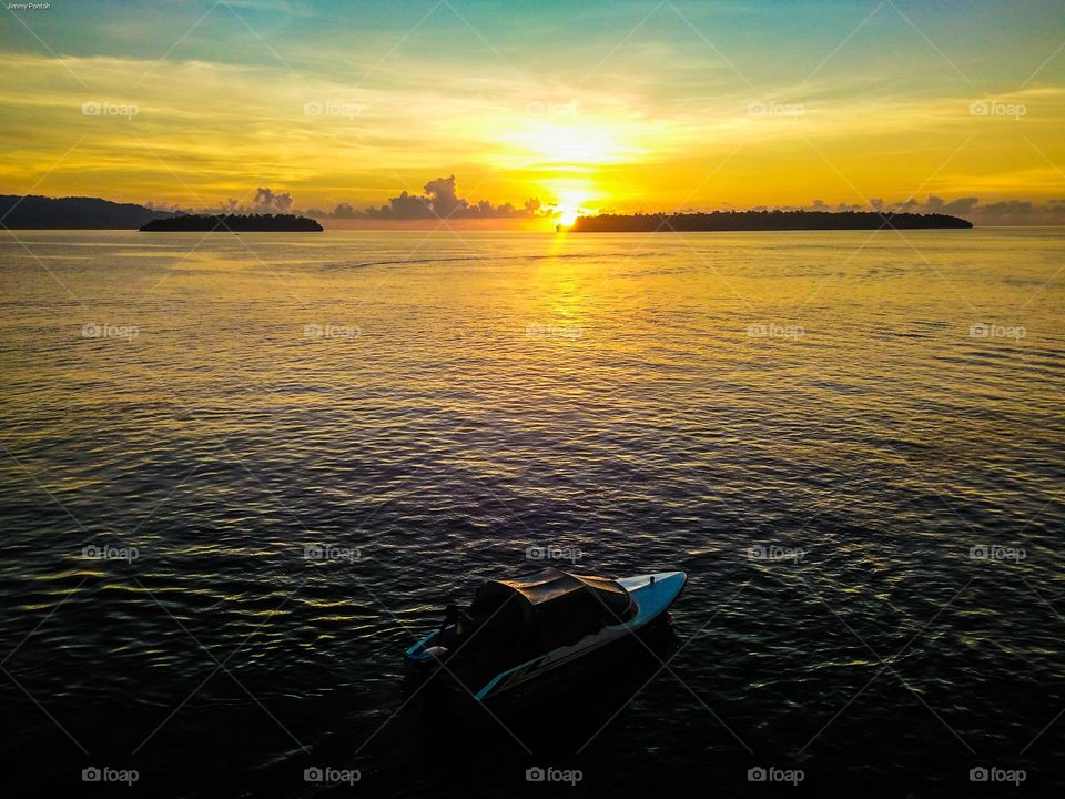 golden coloured sunrise, a speed boat on calm sea water with background two islands in Talaud, Indonesia