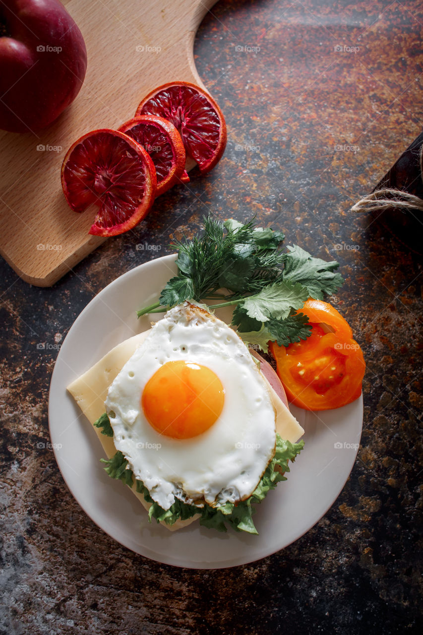 Grain bread with egg, tomato, cheese and bacon on ceramic plate with red orange to desert