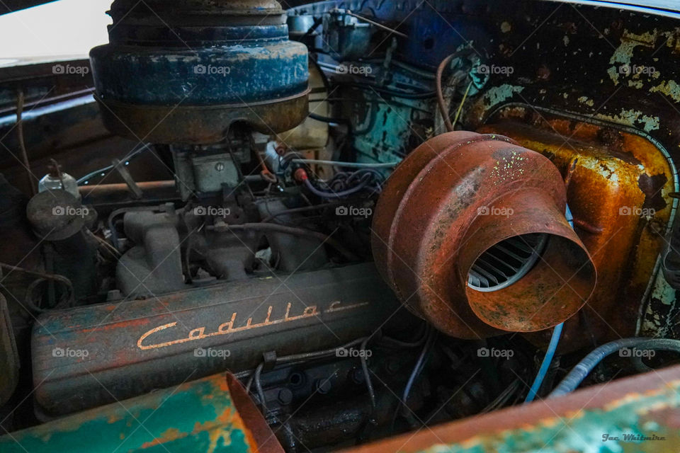 A old Cadillac engine wears a colorful paint scheme with rust acting as one of the primary colors