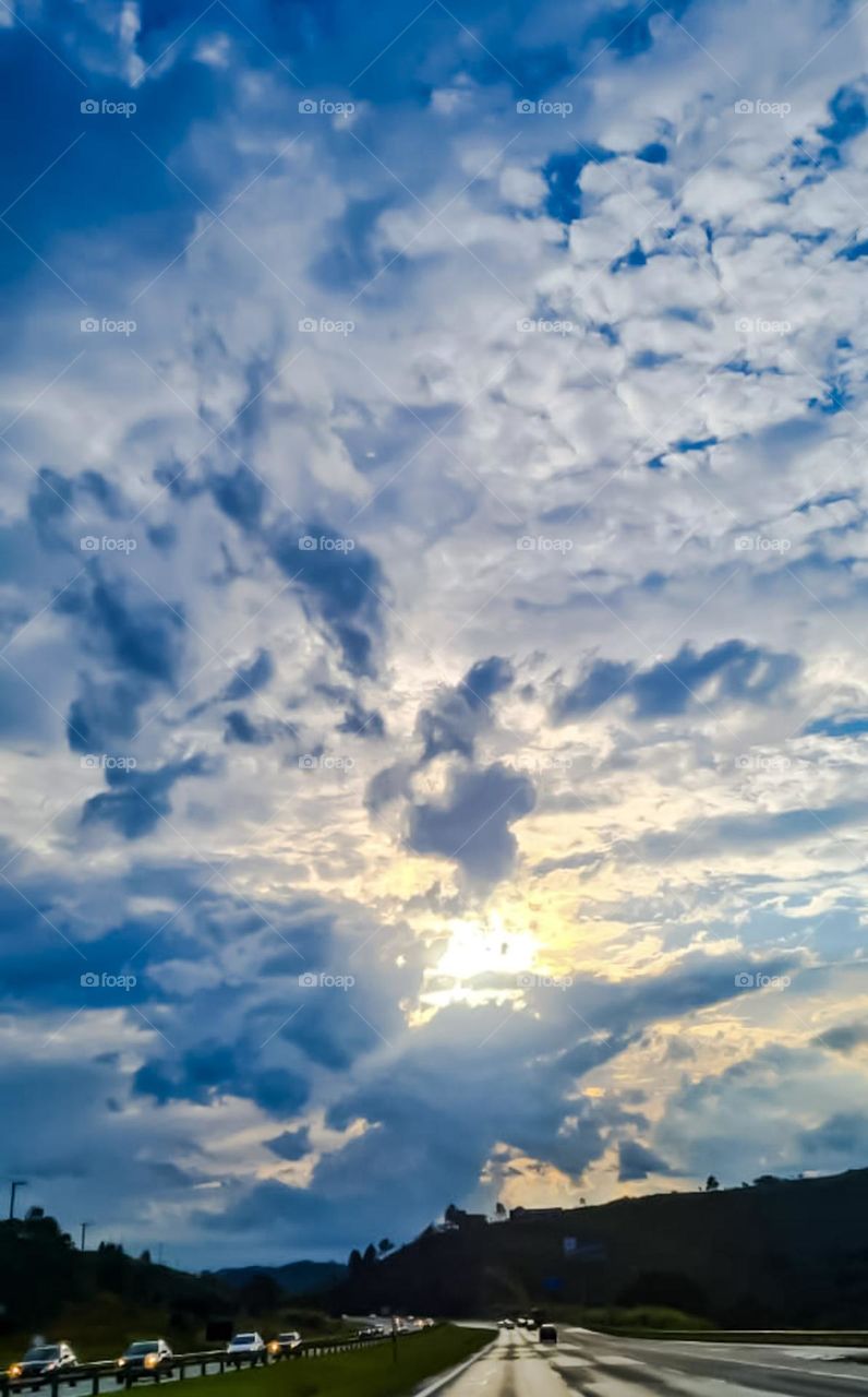 Clouds begin to disperse after heavy rain and the sun's rays already appear on the horizon.  Photo taken on a large highway.
Nuvens começam a se dispersar após forte chuva e os raios solares já aparecem no horizonte.  Foto registrada em rodovia.