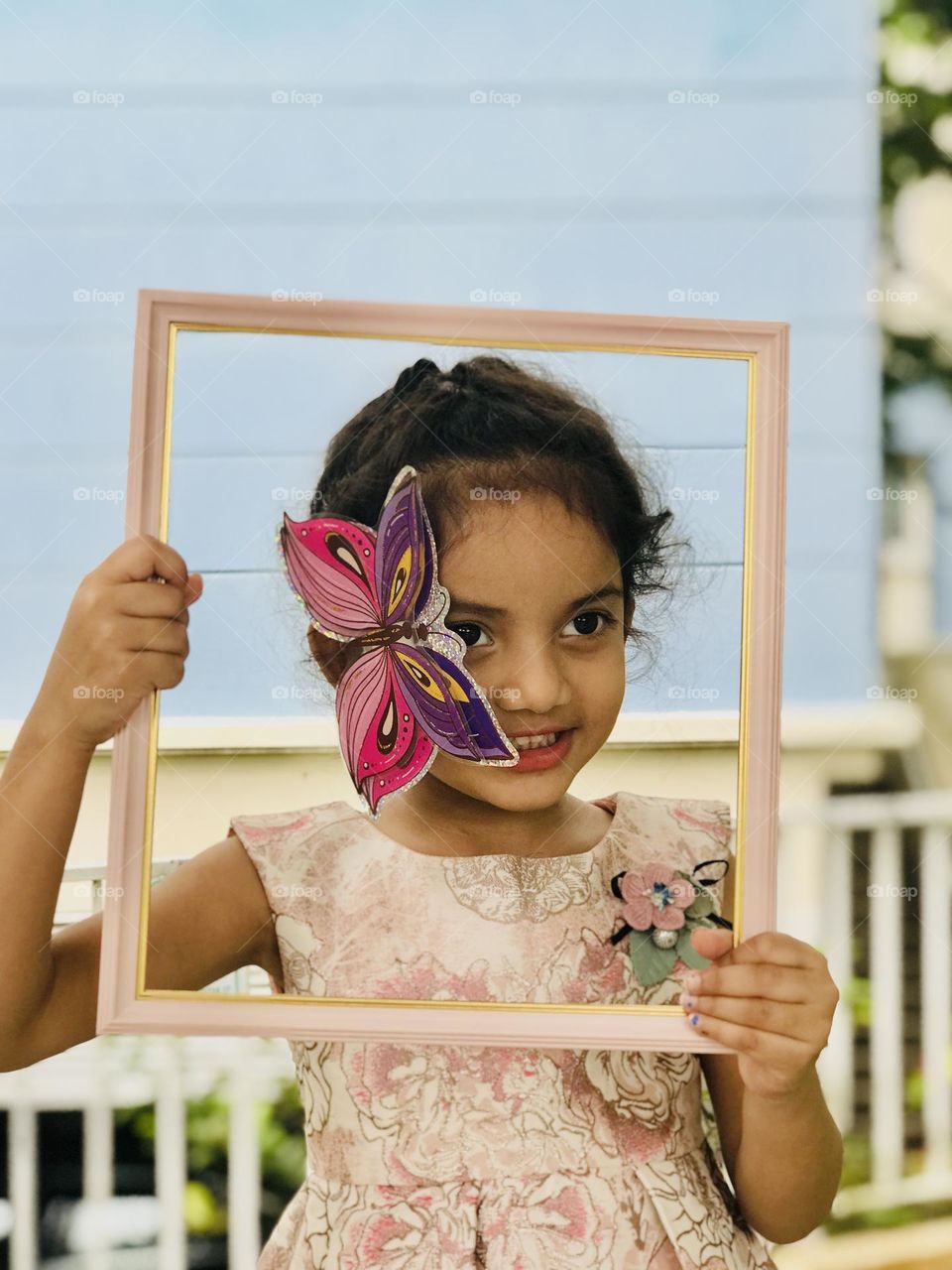 Baby girl in beautiful pink dress and pink butterfly on her face and she holds pink photo frame looks so pretty 😍