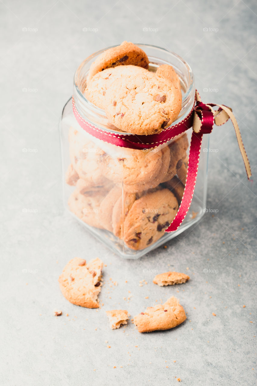 Big jar filled with oat cookies standing on a wooden table. Plain background. Portrait orientation