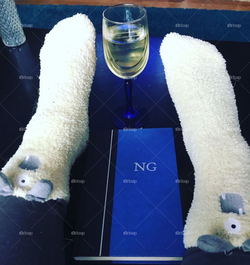 Feet up in fuzzy socks with wine and book