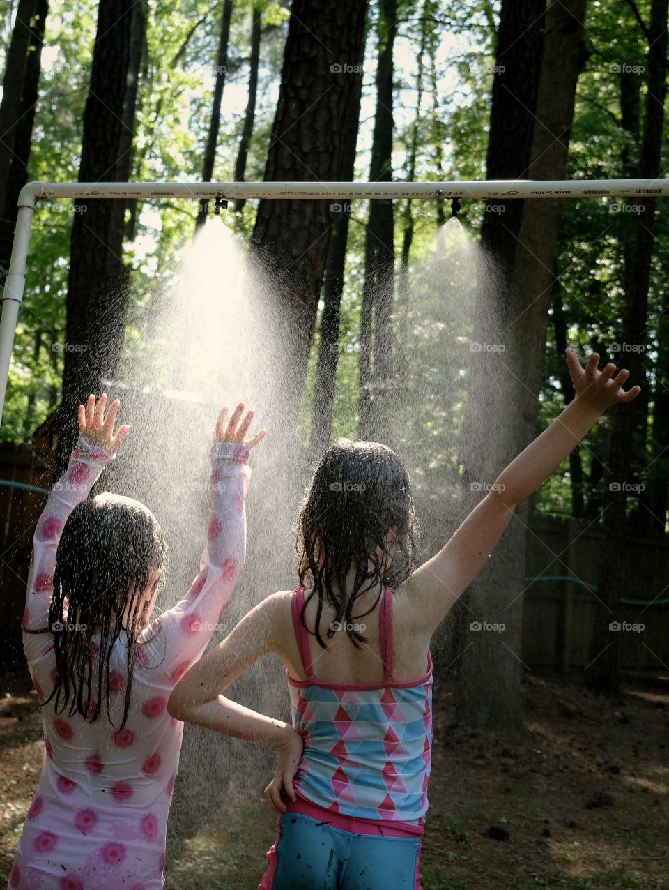 Young sisters playing in the mist on a hot afternoon. 