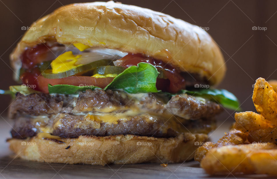 juicy cheeseburger with lettuce, tomatoe, onion, ketchup, mustard on a burger bun sitting next to a pile of French fries
