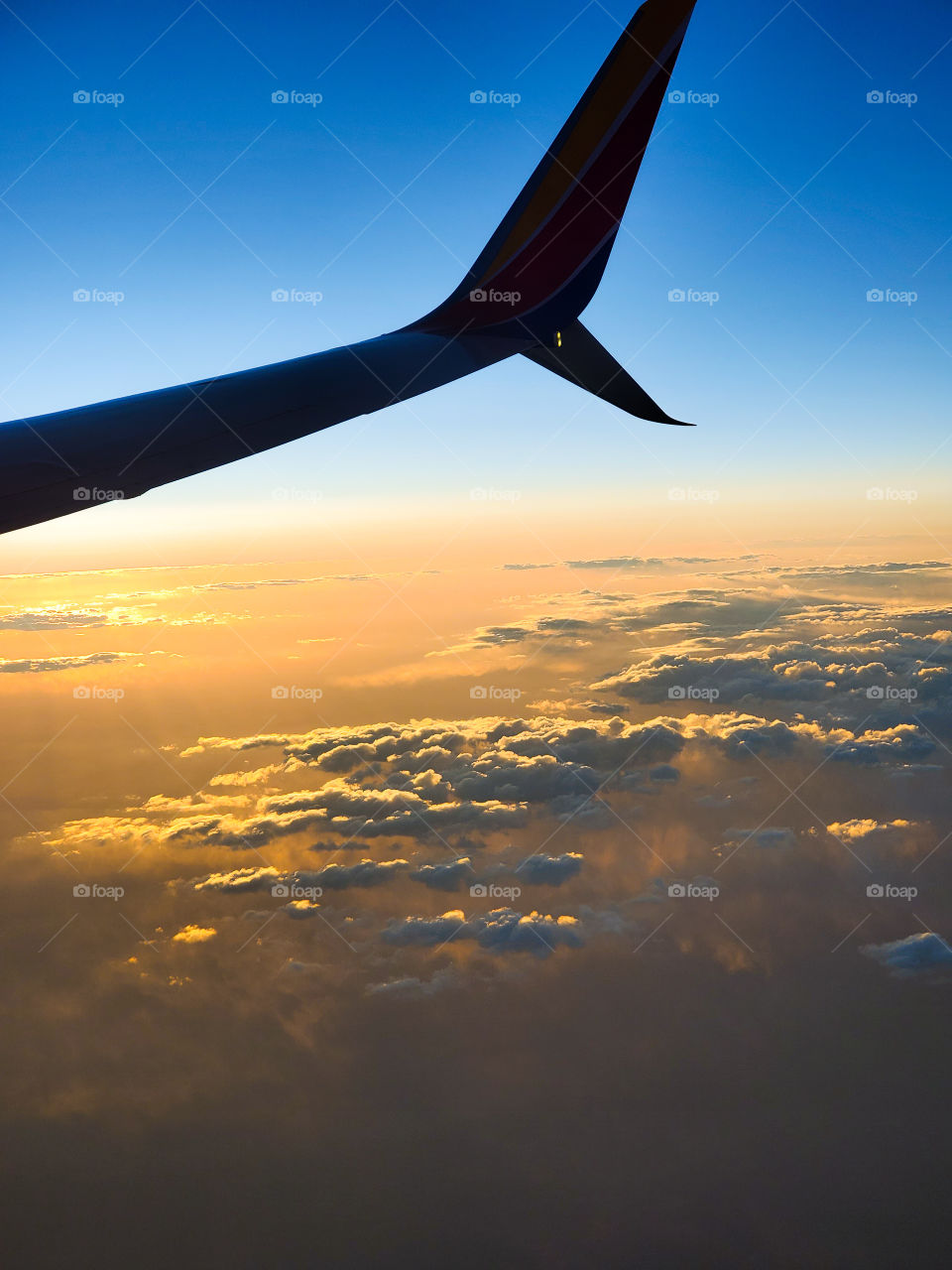 A wing and winglet are contrasted by beautiful orange clouds and blue sky as the sun sets during a cross country flight