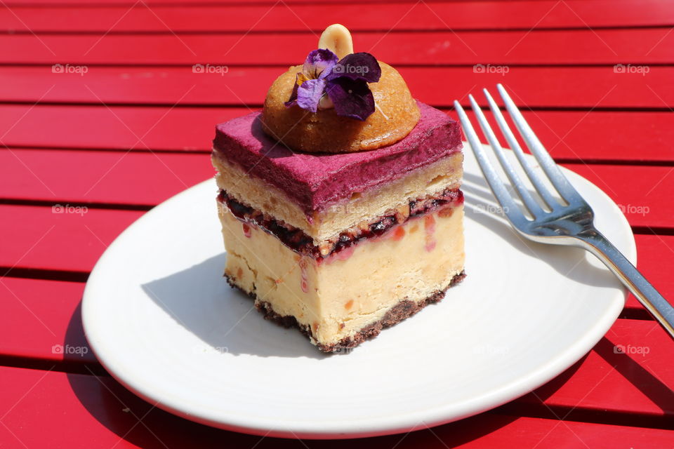 Let’s eat -peanut butter cake with raspberry mousse and edible flower on the top served in a white plate on a red wooden table