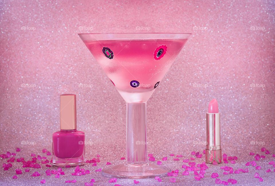 Pink drink with cosmetics against a glitter background.