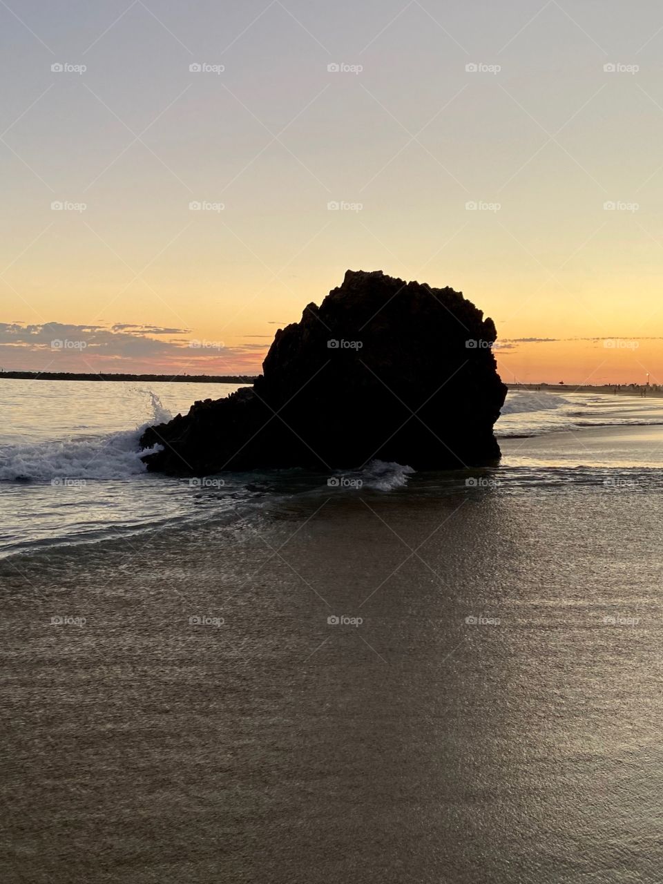 Beautiful sunset at Corona del Mar State Beach with a rock in the background 