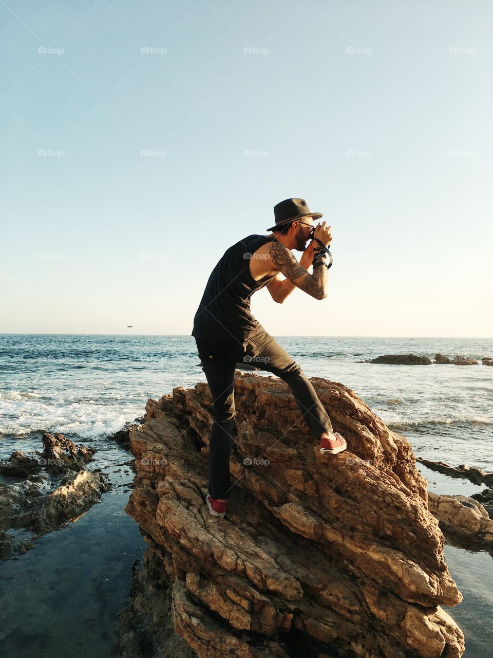 Guy on rocky shore taking photo of sunset. 