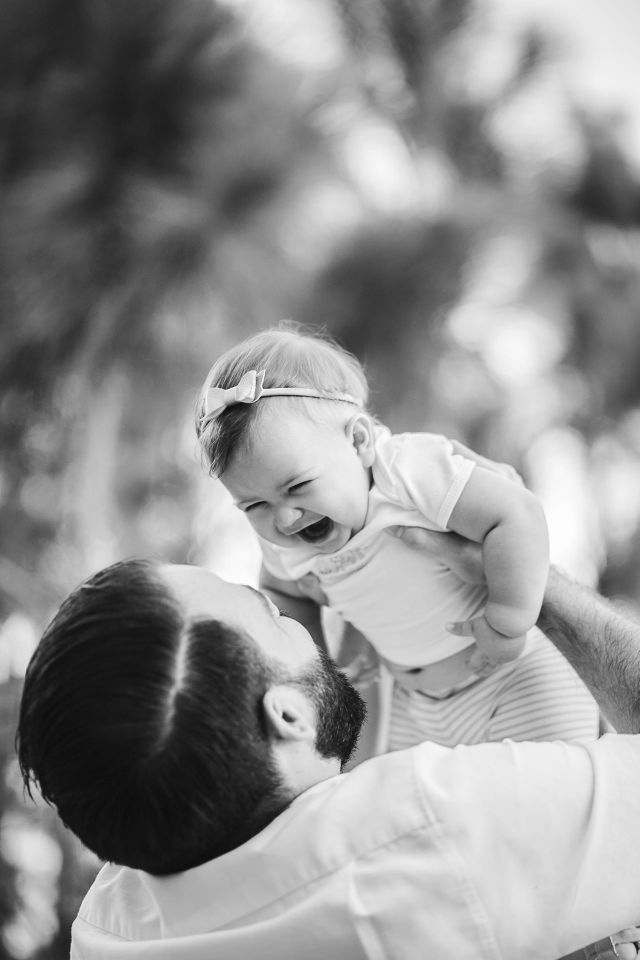 Father playing with his daughter by lifting her up above his head. They both laugh and giggle as they enjoy this sweet moment together.