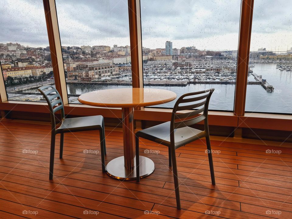 small table with empty chairs in front of large window overlooking the city of Trieste in Italy