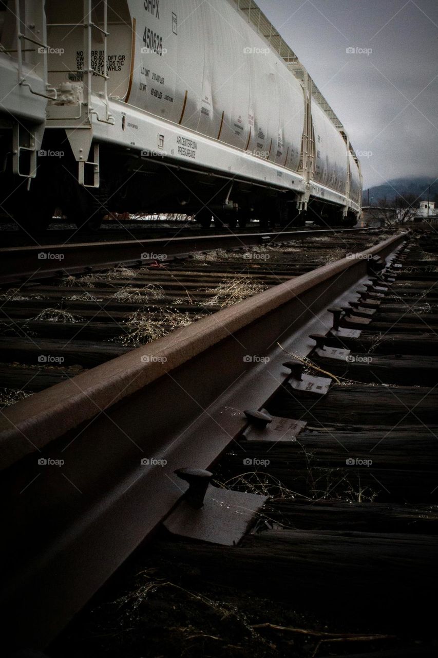 Dark damp train tracks with a series of white train cars in the background in New England.