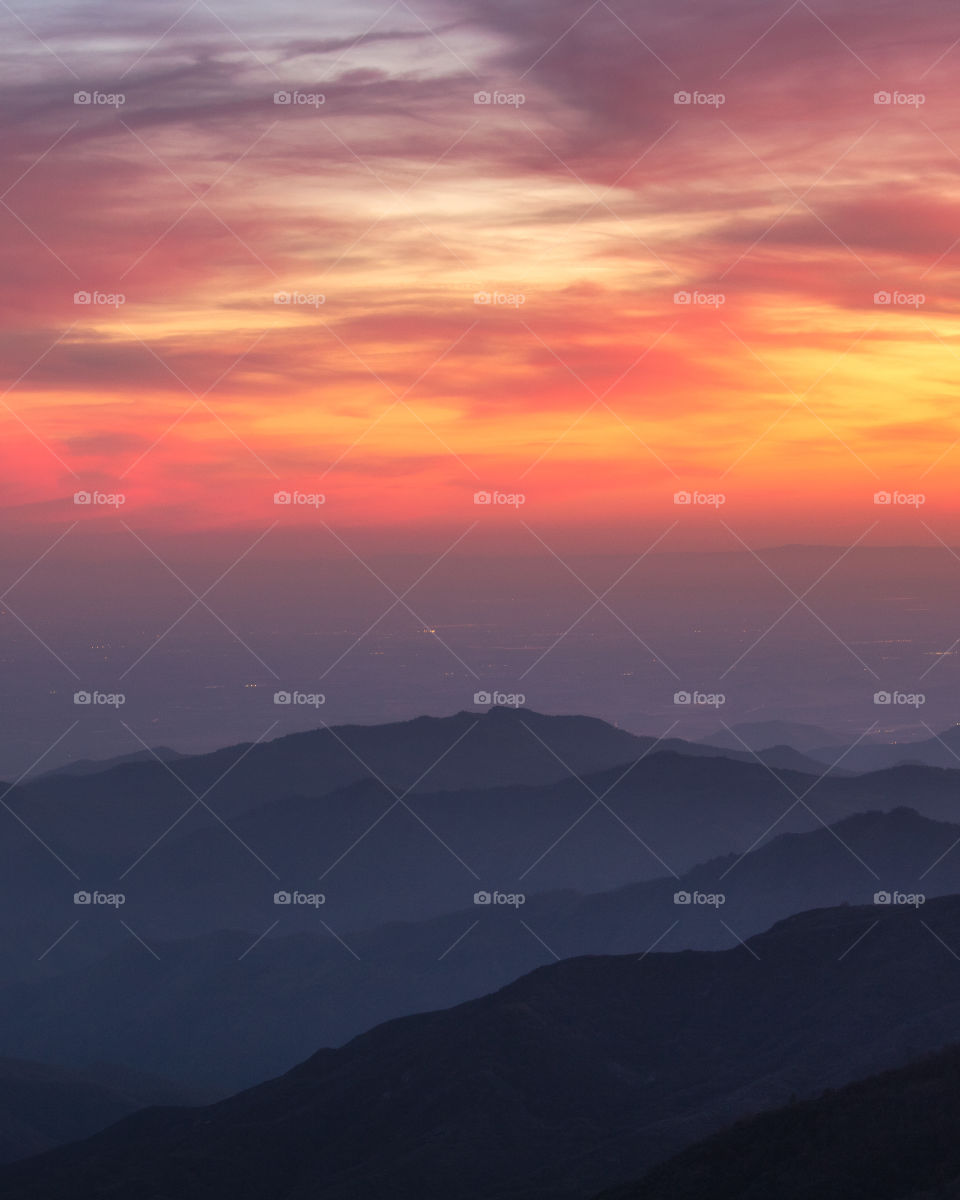 Warm pastel colors in a sunset sky, over layers of ridges in a mountain range. 