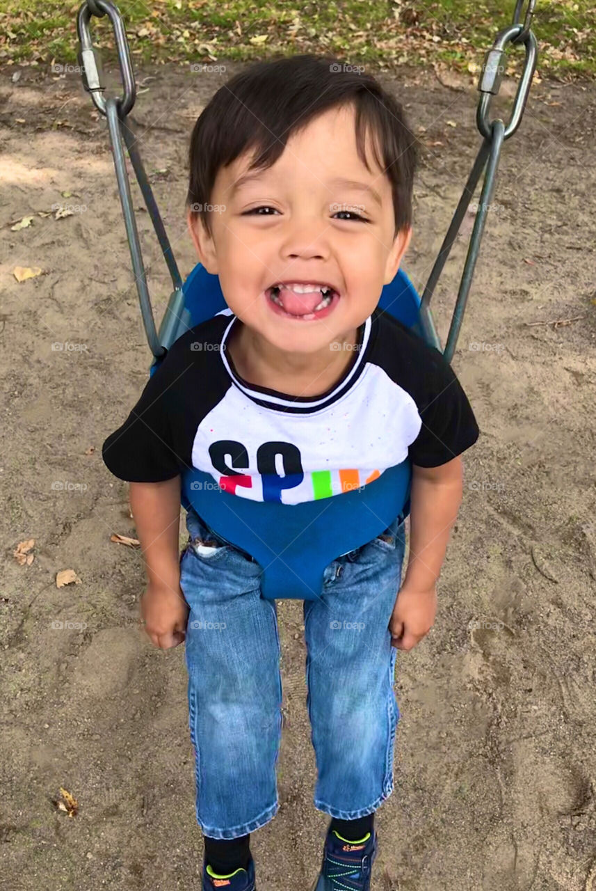 Young boy swinging in the park on a blue swing