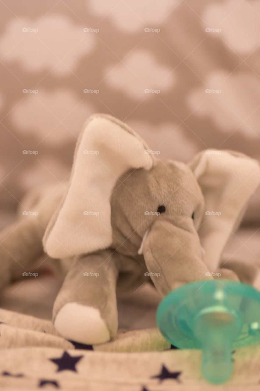 Macro view of stuffed animal elephant and pacifier in baby crib with gray neutral colors