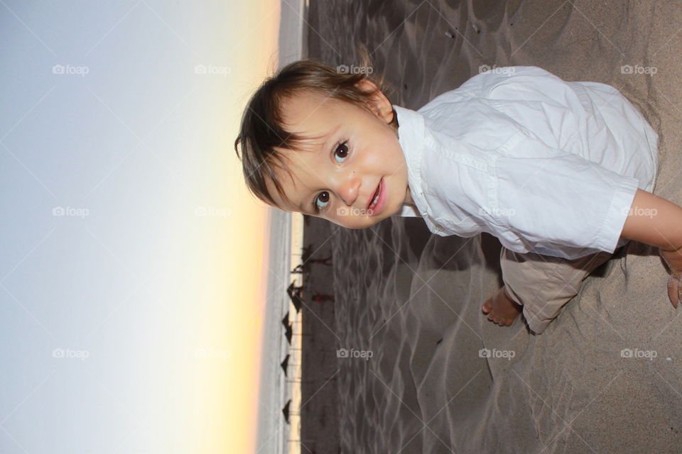 Toddler boy sitting sand in beach during sunset