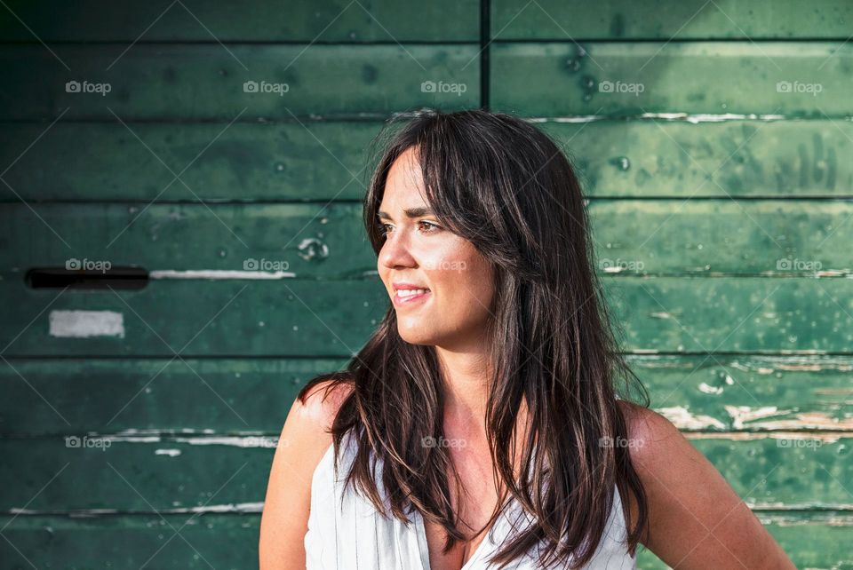 Portrait of beautiful young woman with long dark hair standing in front of wooden green background