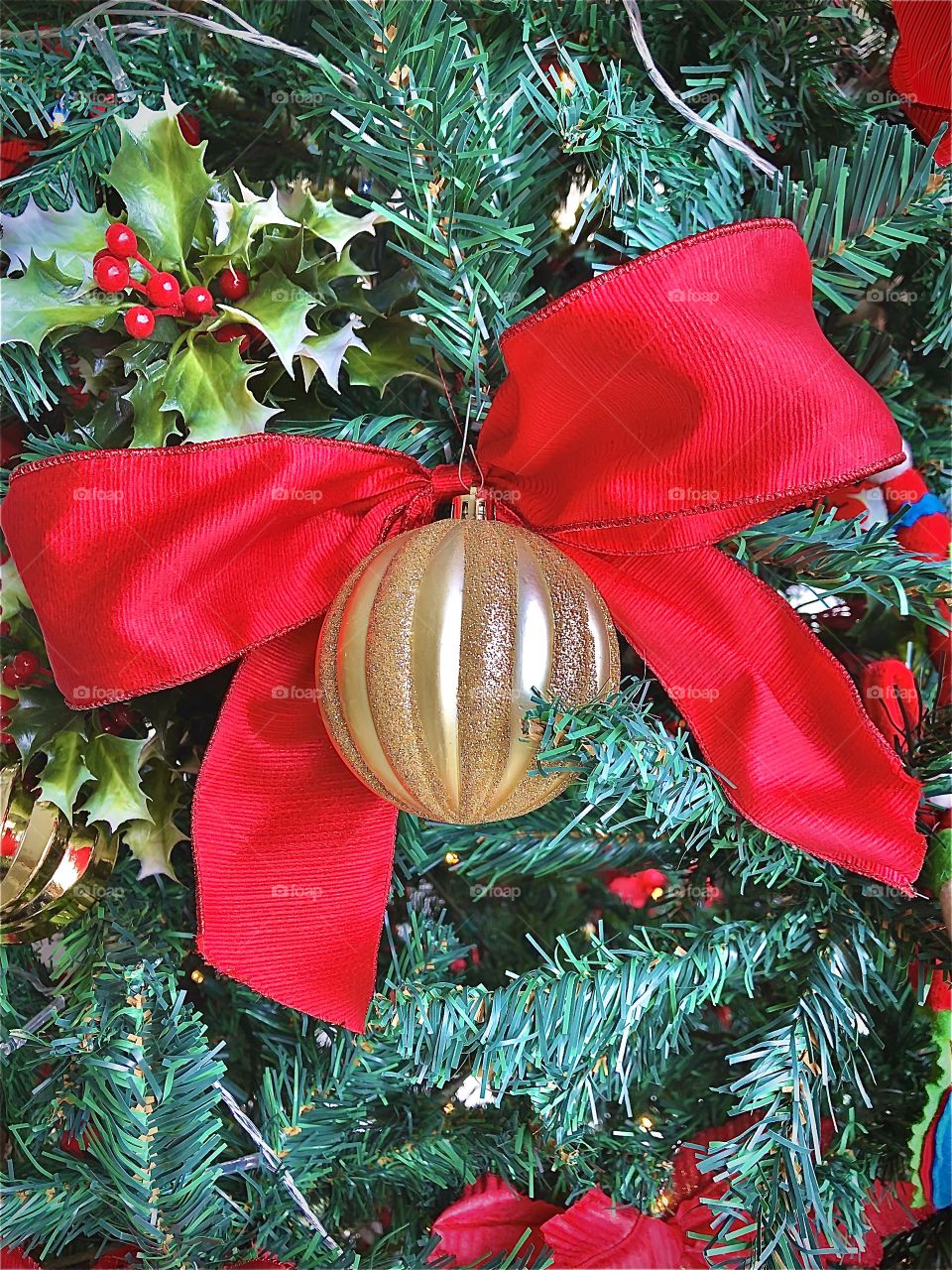 Gold Christmas ball in a decorated Christmas tree with a red bow. 