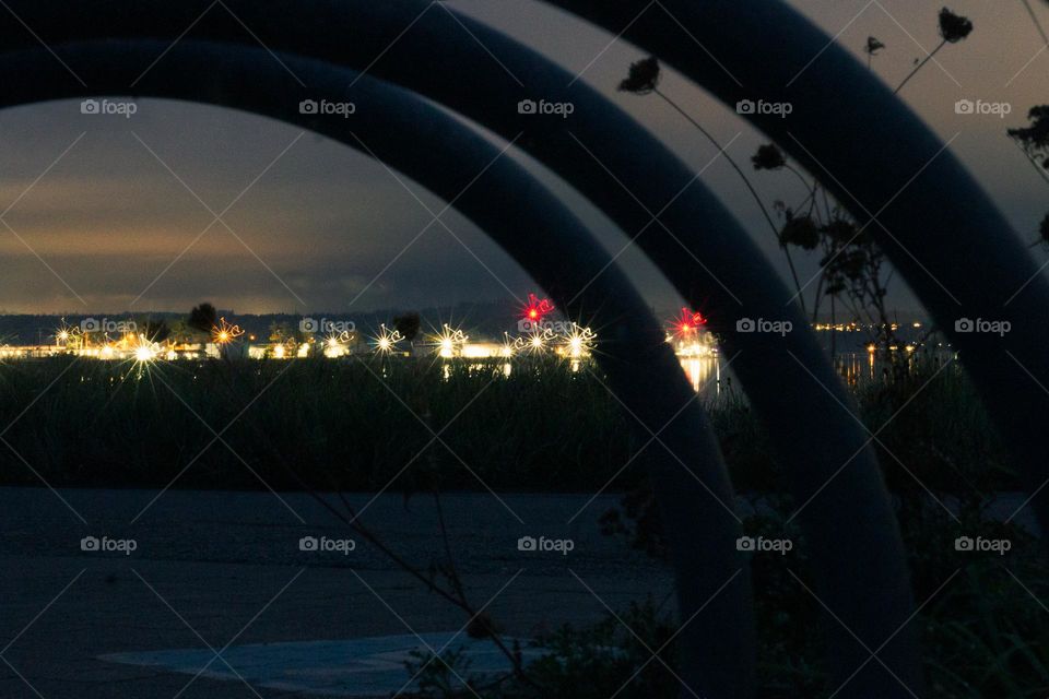 Nighttime shot of marina lights framed through a circular bicycle rack. Soaking in as much light as possible with wide aperture & long shutter speed and a tripod. Marina lights produce interesting shapes that are carried throughout the shot. 