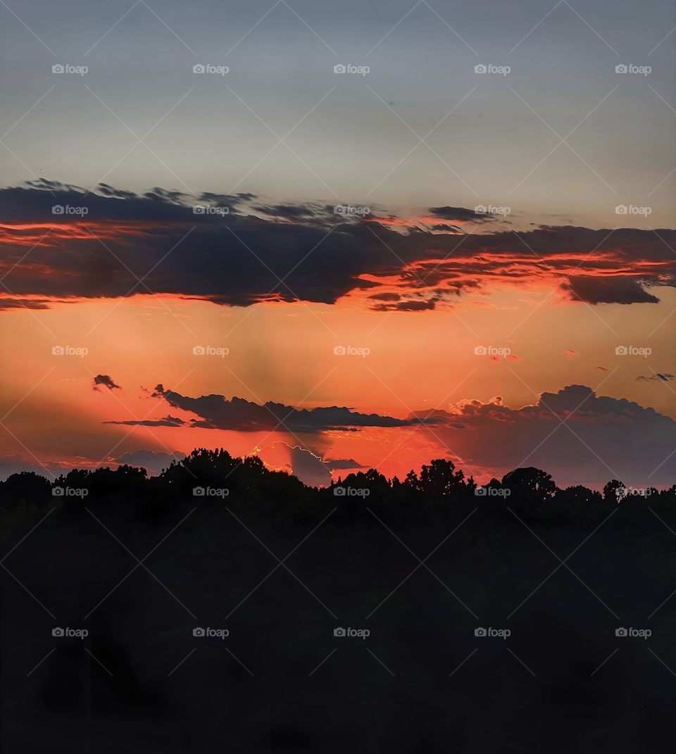 The sun setting in for the evening surrounded by clouds as it gives off an autumn glow.