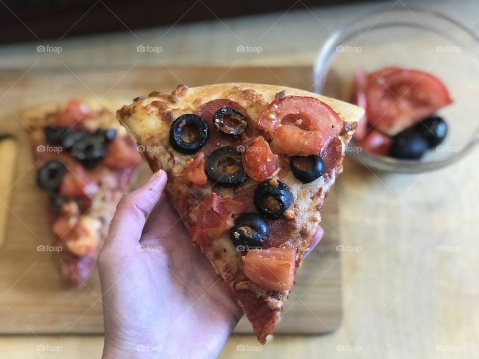 Holding a delicious pepperoni, Olives, cheese and tomato pizza by the cutting board in the kitchen 