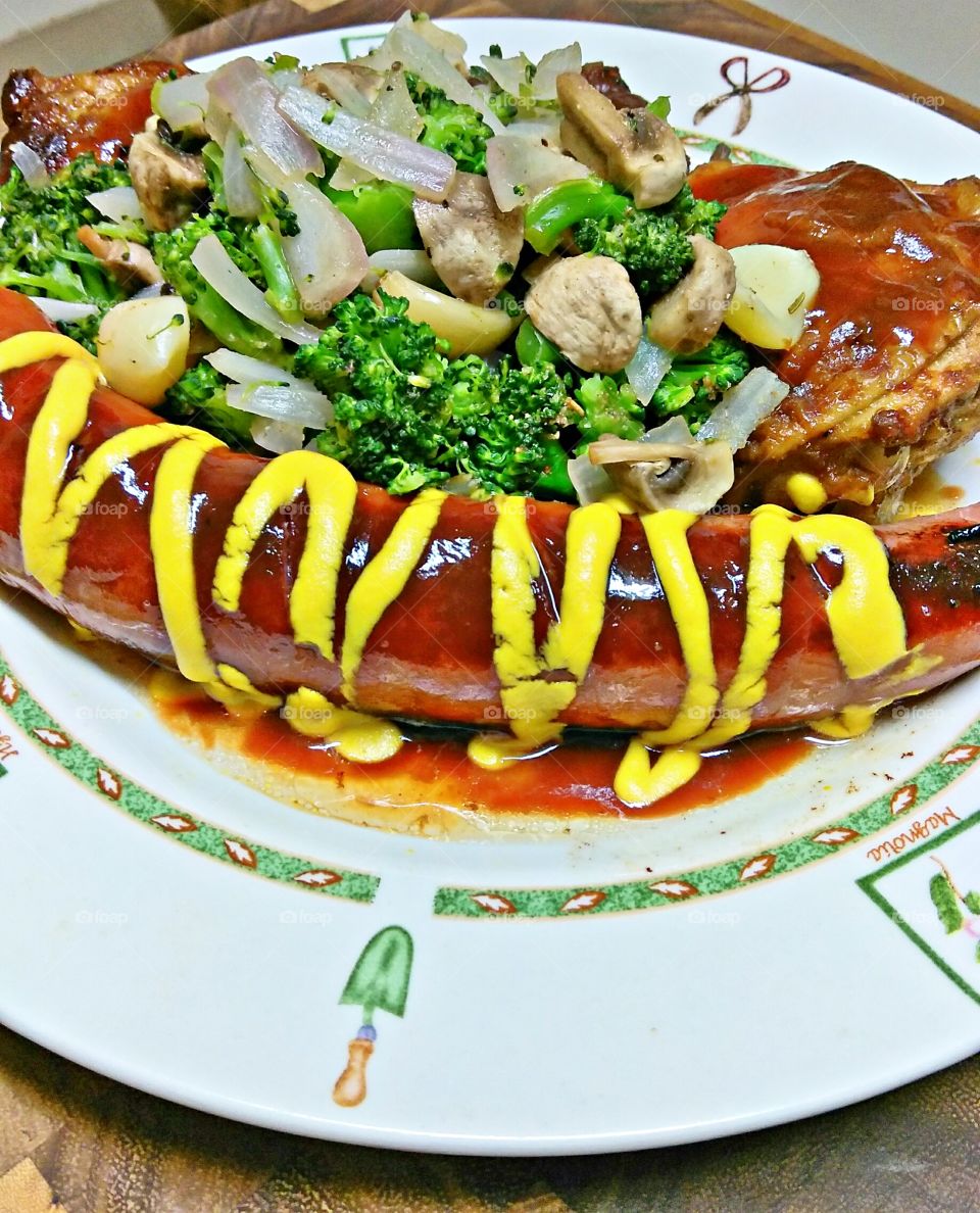 kielbasa sausage with BBQ sauce and mustard with a side dish of broccoli mushrooms and white onions.