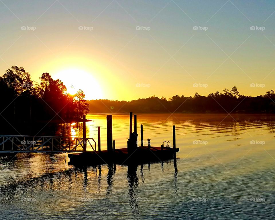 sunrising over a lake with a dock.