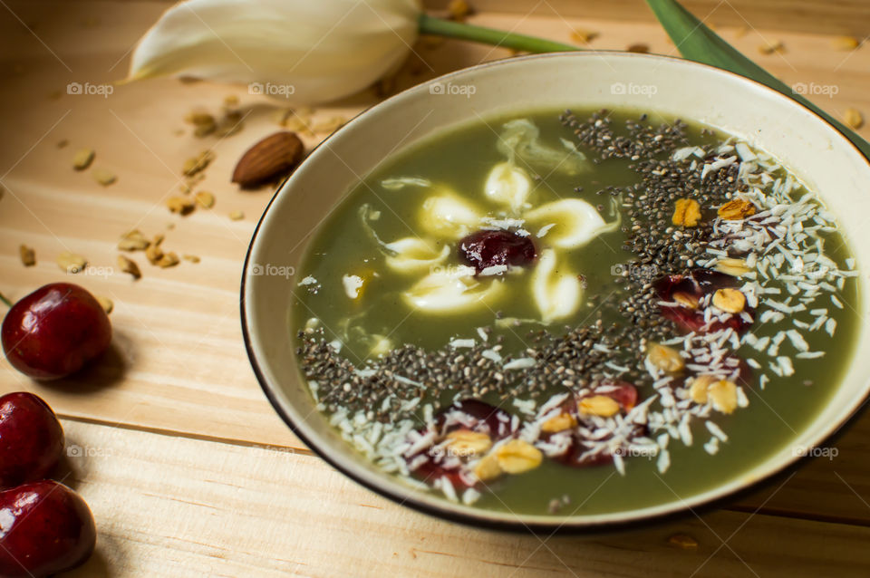 Beautiful green sweet fruit smoothie bowl with coconut,  almond, cherry, chia and white flower design healthy lifestyle artisanal food and drink food photography background 