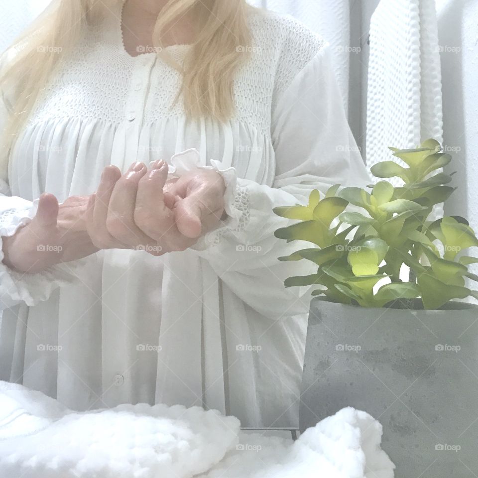 A woman applying lotion to her hands! Wearing white and standing in a white room!