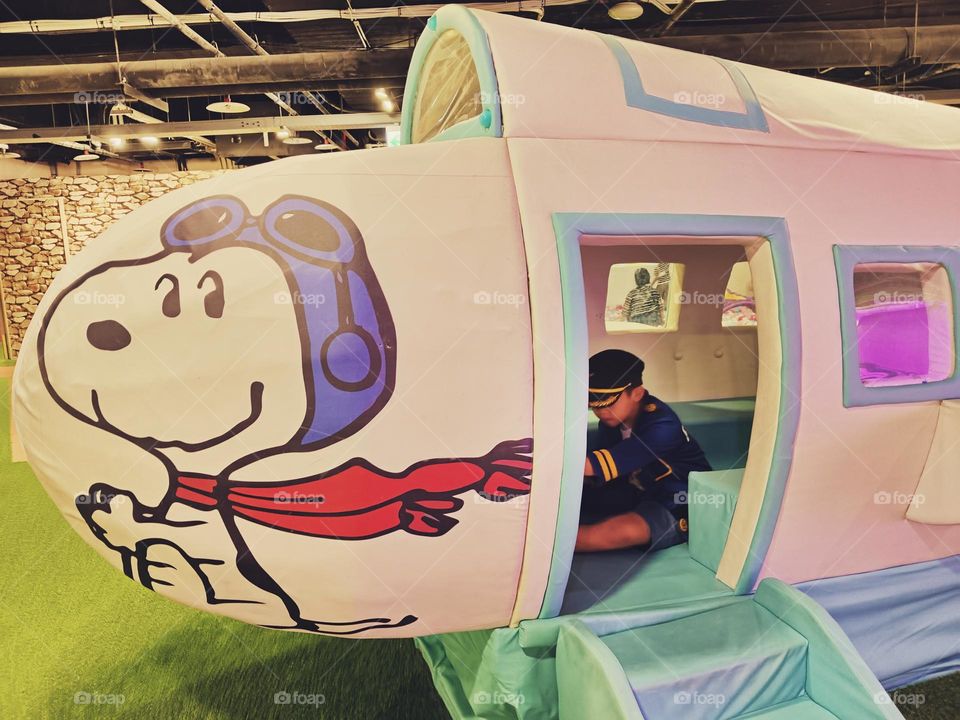 At the amusement park, a little captain pilots a Snoopy airplane, and the overall atmosphere is filled with whimsy and joy.