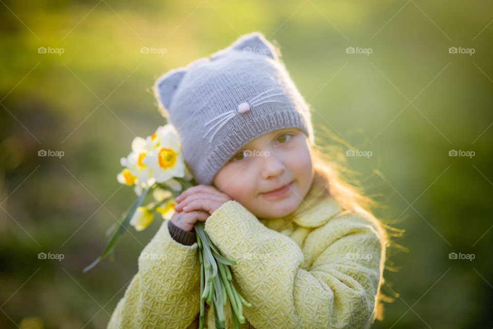 Little girl with narcissus bouquet in spring park