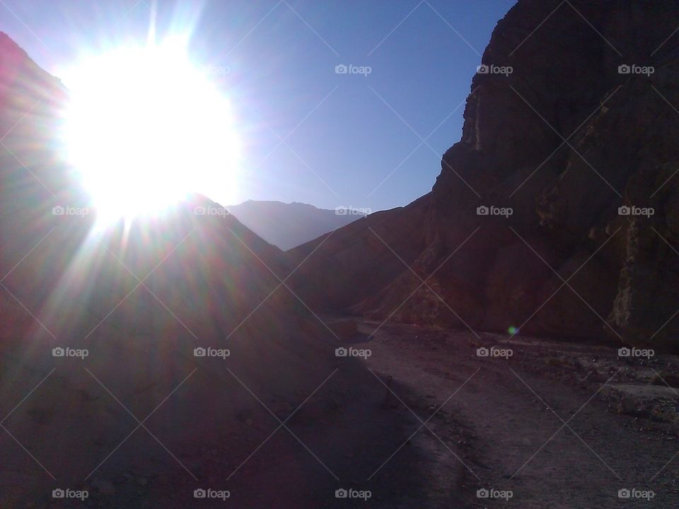 Sun Over Canyon. A view of the sun setting from inside a canyon in Death Valley, with a path winding around.