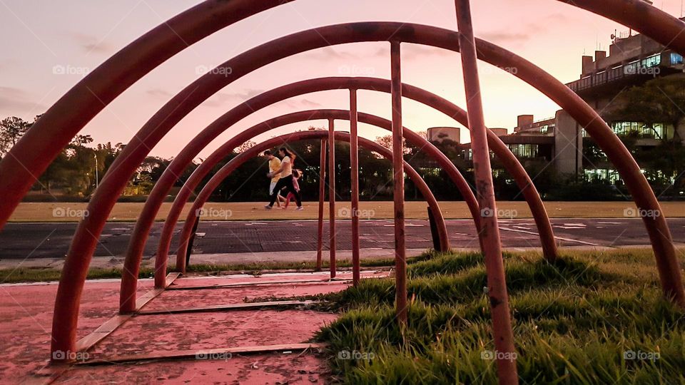 Photo framing through the iron arches of the bicycle parking.  In the background, family walking in the park.