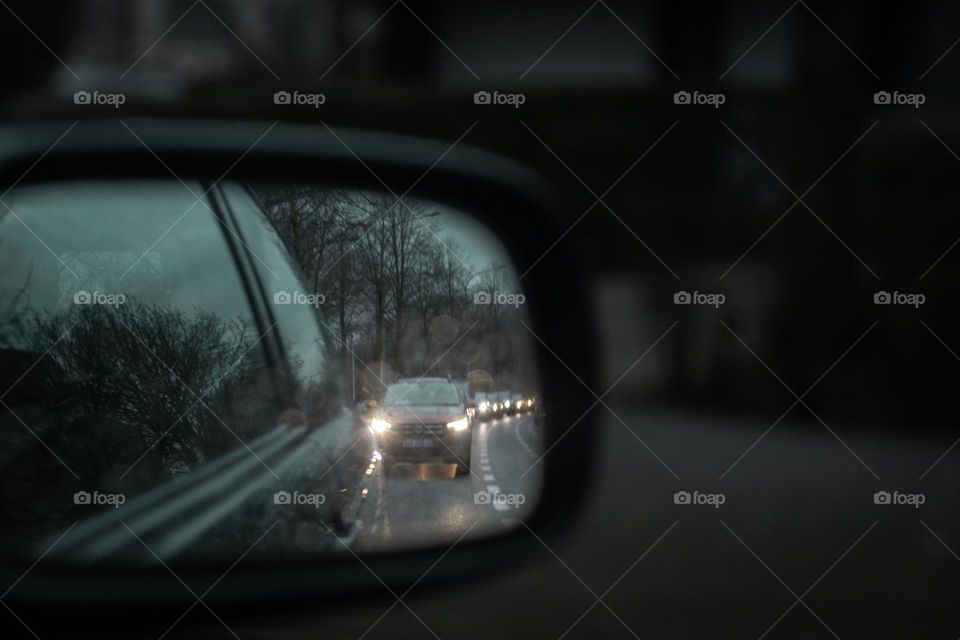Reflection in the rear-view mirror of cars standing in a long queue in a traffic jam on a city street in the evening, side view close-up.