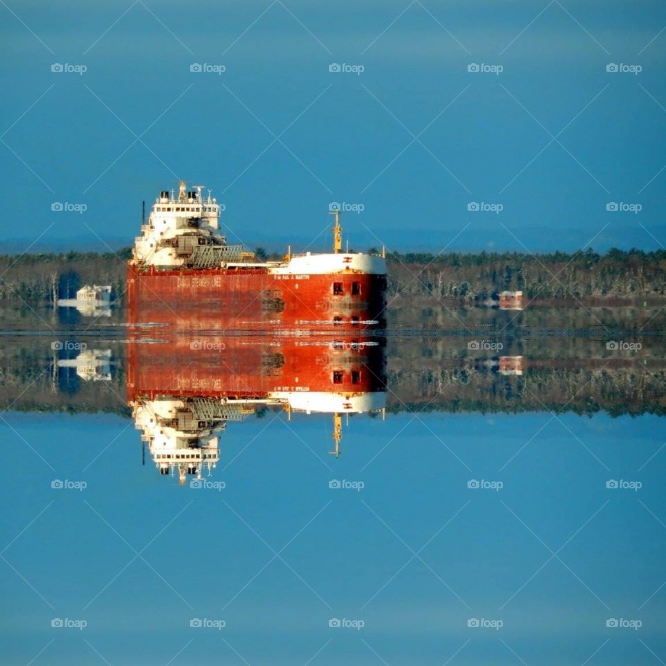 freighter ship on the st. Mary's River in sault Sainte Marie Michigan. The sky is a perfect blue and the water perfectly still making for a great reflecting photo.