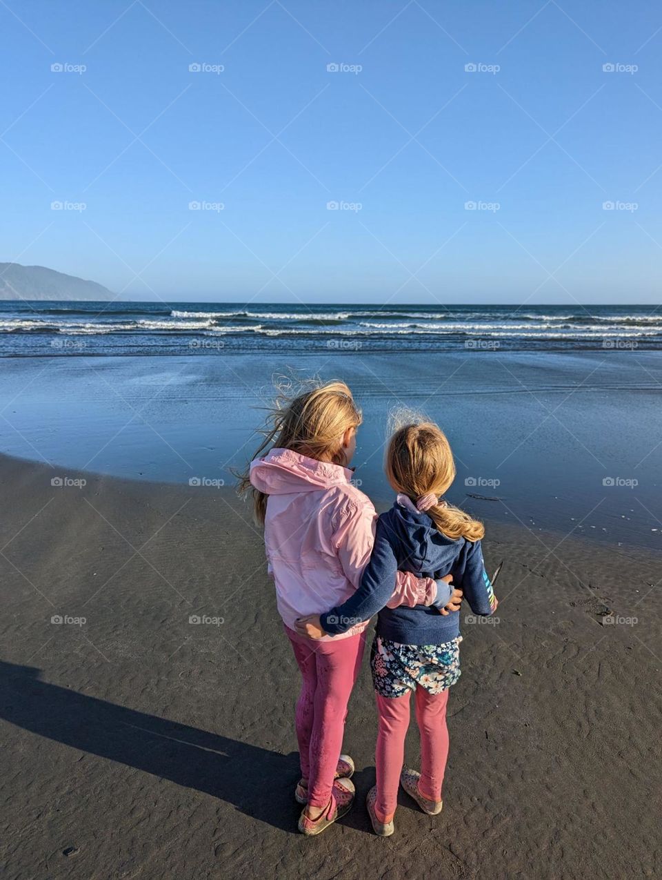 sisters with arms around each other enjoying a quiet moment of peace together watching the ocean waves