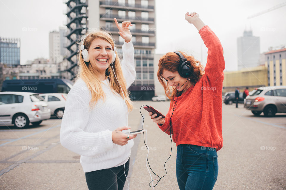 two beautiful women friends dancing happy in the street with headphones and smartphone