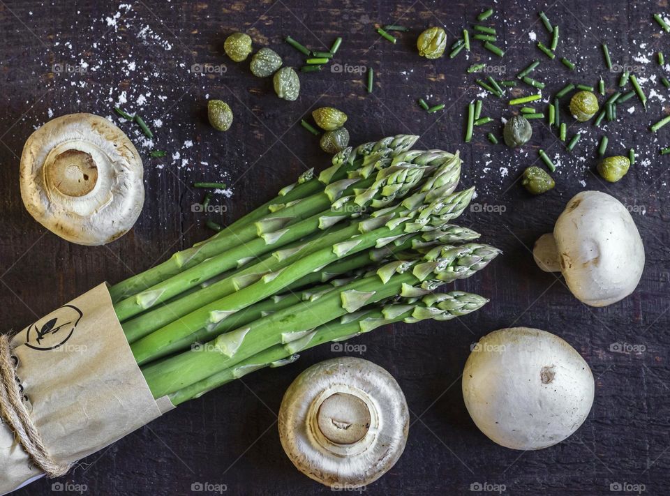 Fresh asparagus and mushrooms on a dark wood board with chives, capers & salt