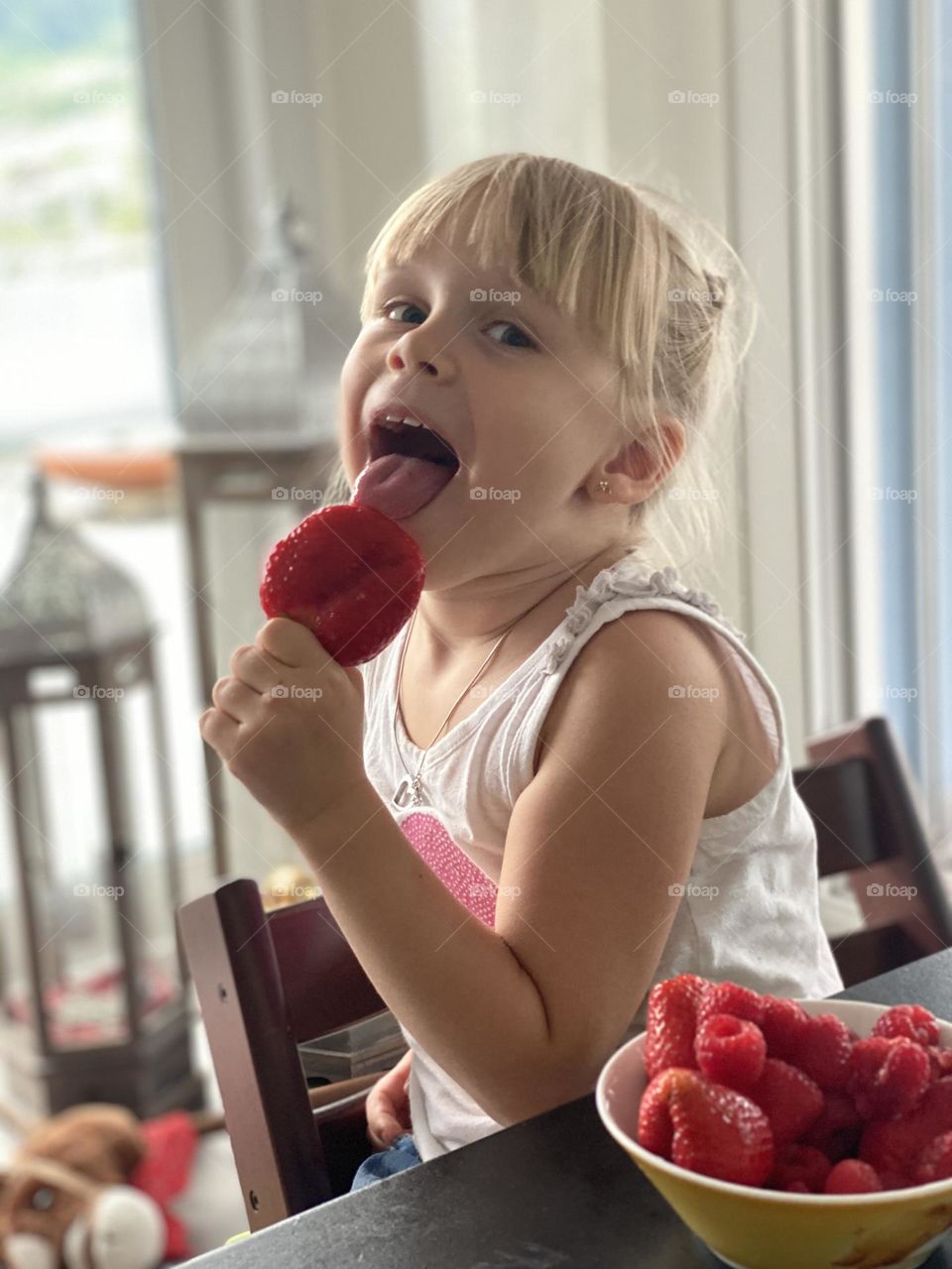 delicious summer red berries strawberries with raspberries enjoyed by a little girl child blonde at the table