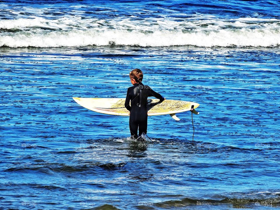 Boy with his surfboard in the waves of Pacifica, California