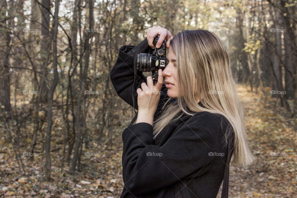 Beautiful blonde woman taking pictures in the forest