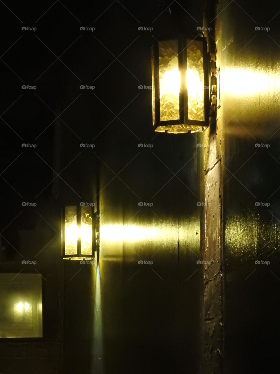 Wall lights and light fixtures seen in a perspective in an Italian restaurant with dark atmosphere with reflection of the lighting on the paper painted wall.