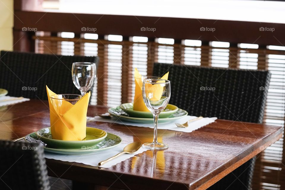 wooden table and seat at the restaurant. well prepared table with dishes and napkins. selective focus on the glass of wine. Window lighting.